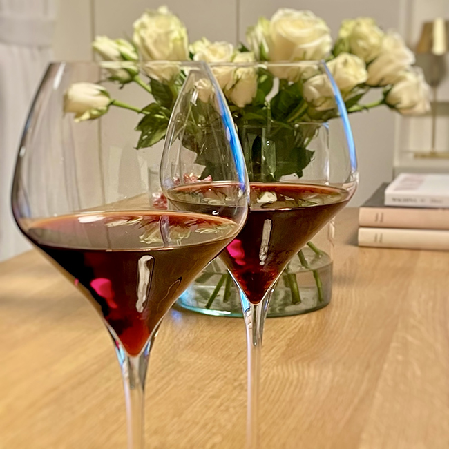 Due calici di vino rosso in primo piano su tavolo con fiori freschi