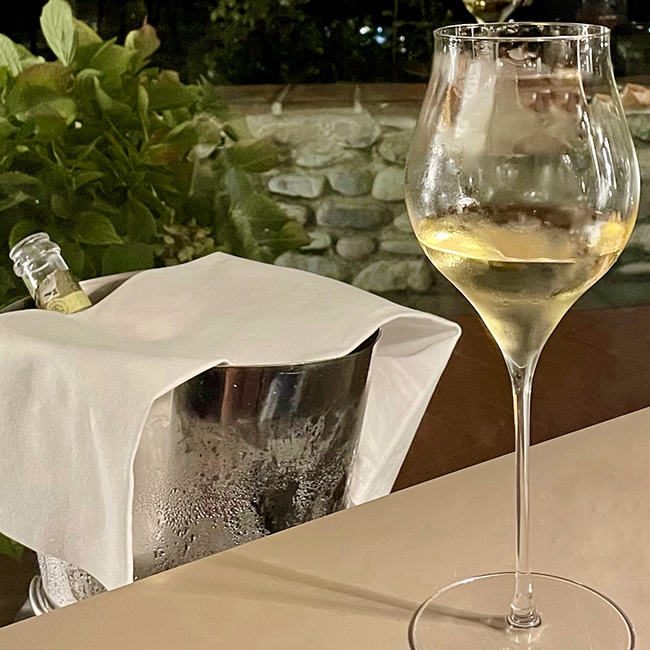 Calice di vino spumante servito freddo accanto a un secchiello con bottiglia