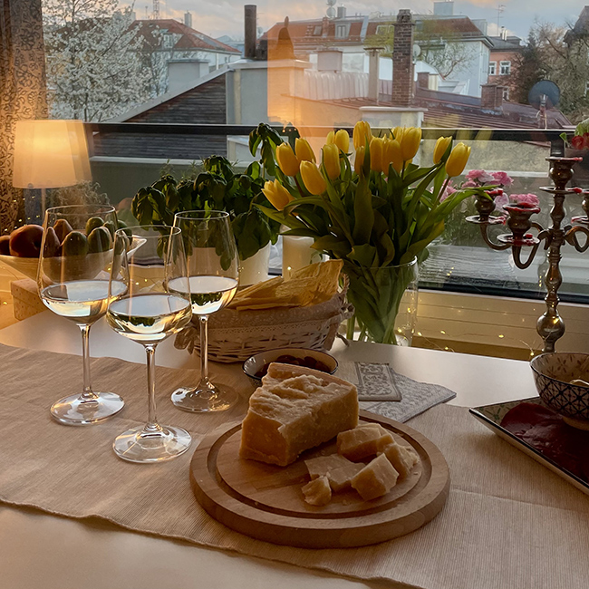 Tavola imbandita con calici di vino bianco, Parmigiano Reggiano e decorazioni floreali in una terrazza elegante al tramonto