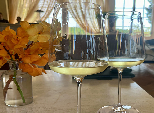 Due calici di vino bianco serviti in ambiente elegante con luce naturale